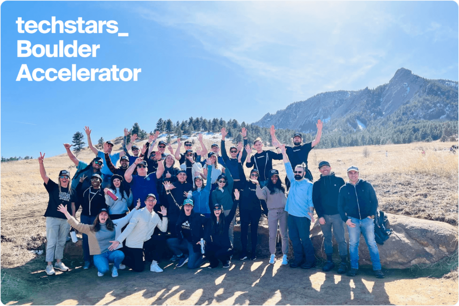 A picture of a group of the 30 members of the Techstars Boulder March 2024 cohort raising their hands in front of a mountain landscape